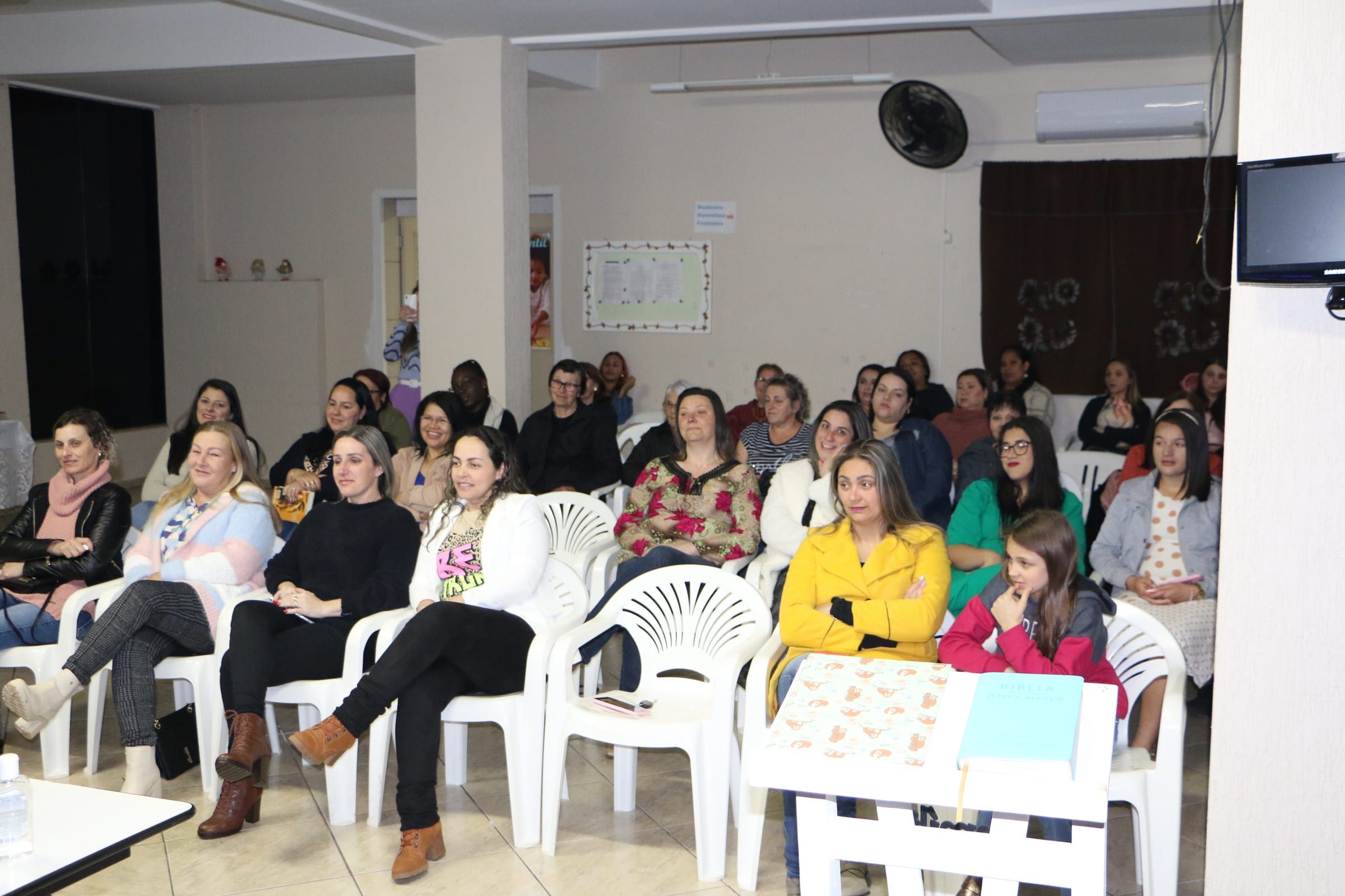 Mulheres sentadas, sorrindo, em um encontro da igreja.